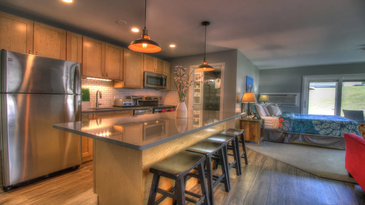 A modern suite combining a kitchen island, stainless steel appliances, casual bedroom area, and decorative touches like a vase with flowers and ambient lighting. The space appears open and multifunctional, ideal for relaxing, socializing, or preparing a meal together after a day of adventure.