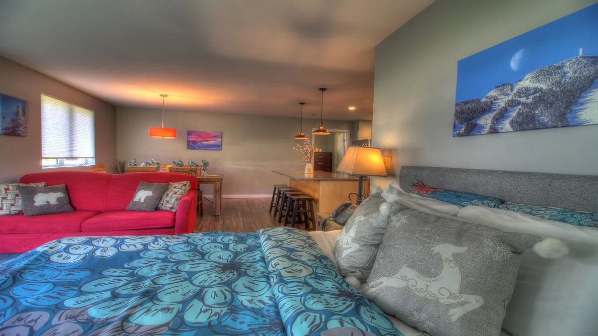 A comfortable living area with a red sofa adorned with decorative pillows, dining area in the background, and creative artwork on the walls. The scene feels warm and invites conversation, laughter, and intimate gatherings among friends or couples.