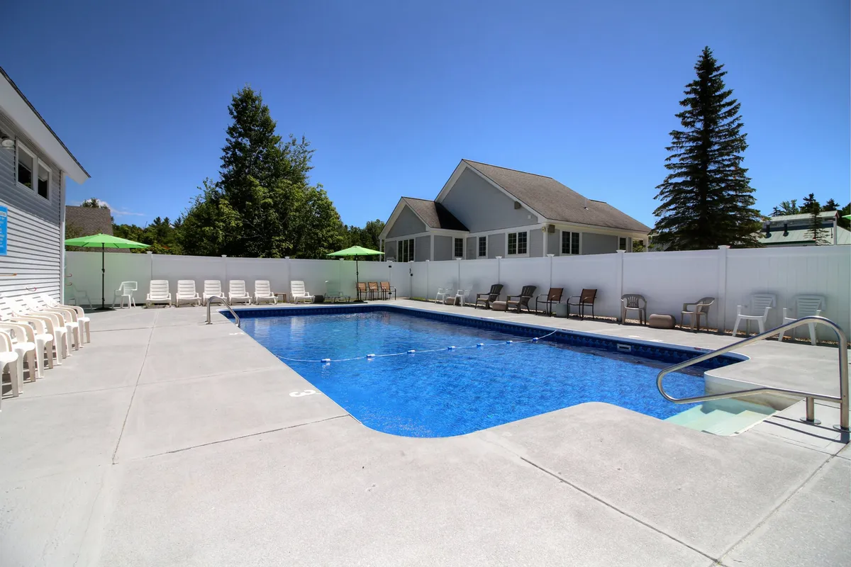 An exterior pool area with sparkling blue water, lounge chairs, umbrellas, and surrounding greenery. The setting is perfect for swimming, sunbathing, relaxing, or socializing, capturing the laid-back vibe of resort-style amenities right on site.
