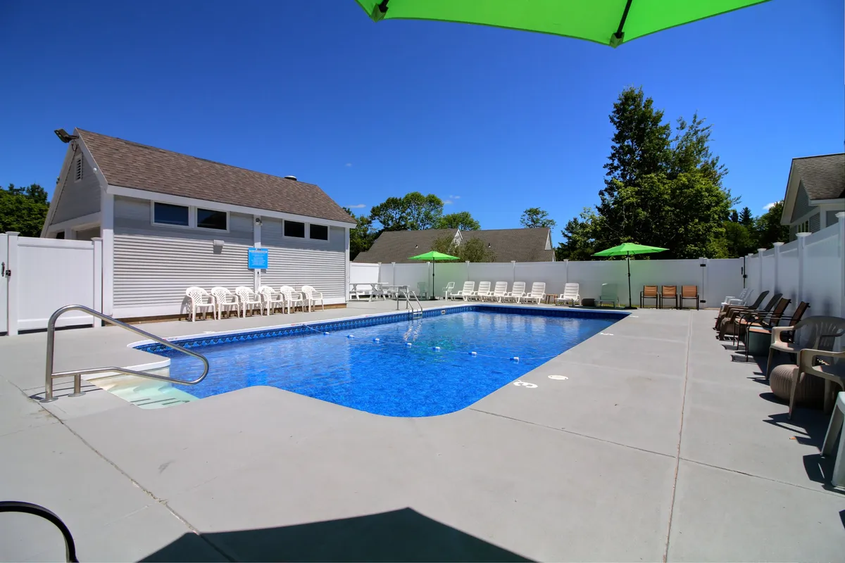 A vibrant outdoor pool scene featuring green umbrellas and inviting lounge chairs arranged around a sparkling pool. The relaxed atmosphere suggests sunbathing, swimming, and poolside meals or barbecues under the open sky.