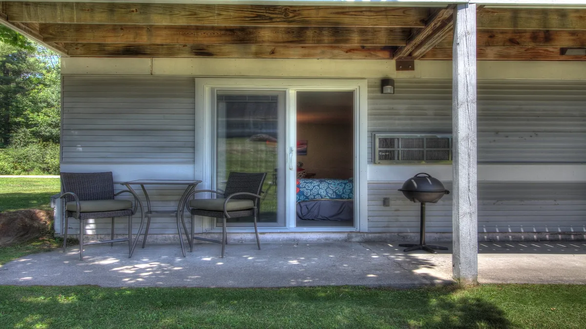 This image shows a cozy patio area just outside a sliding glass door, featuring comfortable seating and an electric grill. The space is surrounded by greenery, inviting guests to relax, dine al fresco, or enjoy a peaceful morning coffee.