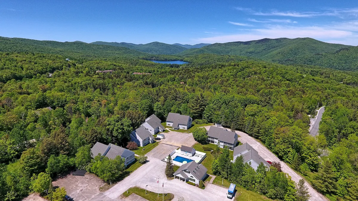 This exterior image captures a serene setting featuring a sparkling swimming pool surrounded by a cluster of buildings nestled amidst lush greenery, with the majestic mountains forming a scenic backdrop. The scene evokes an atmosphere of relaxation, adventure, and connection to nature.