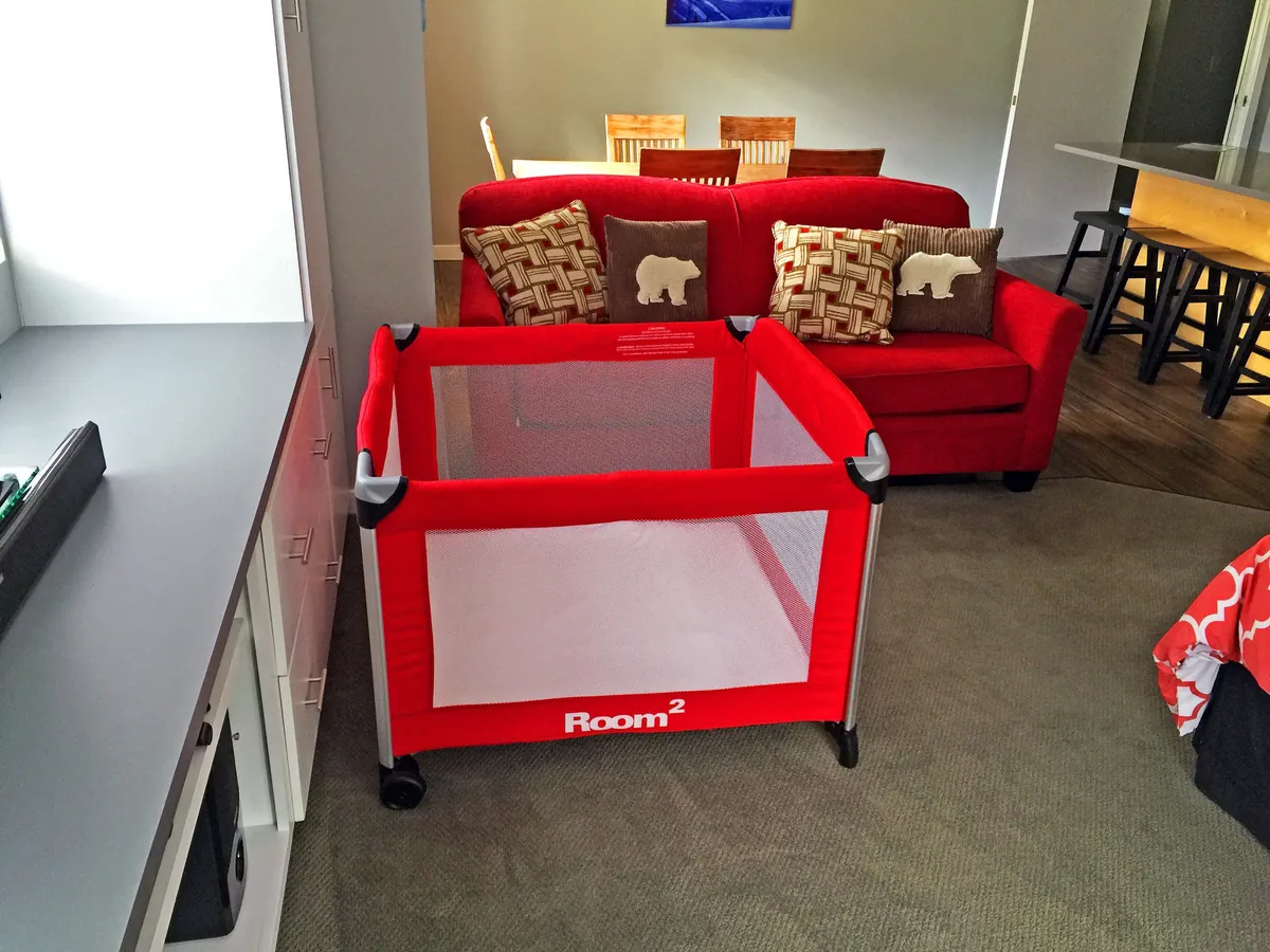 A warm, family-friendly living area is shown, featuring a red couch, dining table, and a playpen, suggesting a space that caters to relaxation, family gatherings, and play. The arrangement supports both casual seating and communal dining, hinting at the versatility and comfort described in the section.