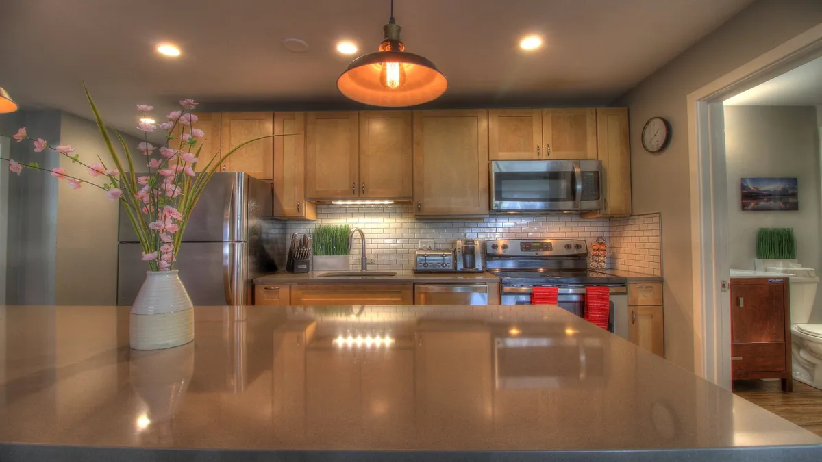 This shot centers on a modern kitchen featuring a generous island with seating for four, a flower vase as a welcoming centerpiece, and gleaming stainless steel appliances. The scene is ready for entertaining or family meals, emphasizing the culinary and social functions of the space.