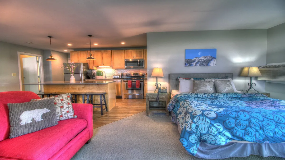 A welcoming open-plan area with a kitchen island, colorful bedspread, and a red accent chair. The kitchen is well-equipped for meal prep and socializing, complementing the suite’s family-friendly layout.
