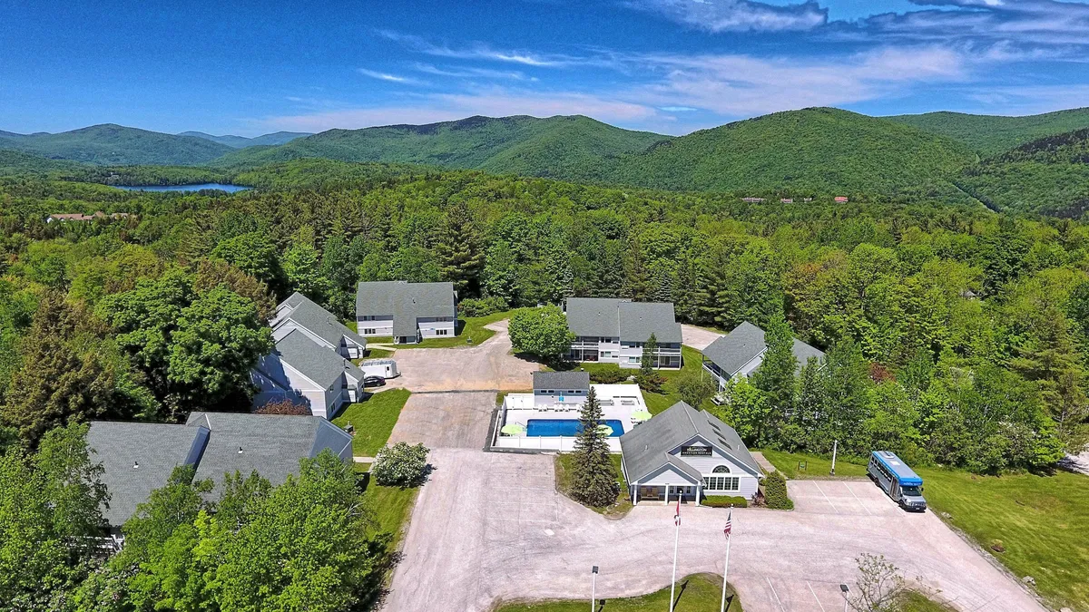 This image showcases a striking exterior view of the Suites at Killington with a mountainous landscape forming the backdrop. The inviting swimming pool and cluster of buildings are visible, set against the natural beauty of the surroundings, even though the pool is closed in winter.