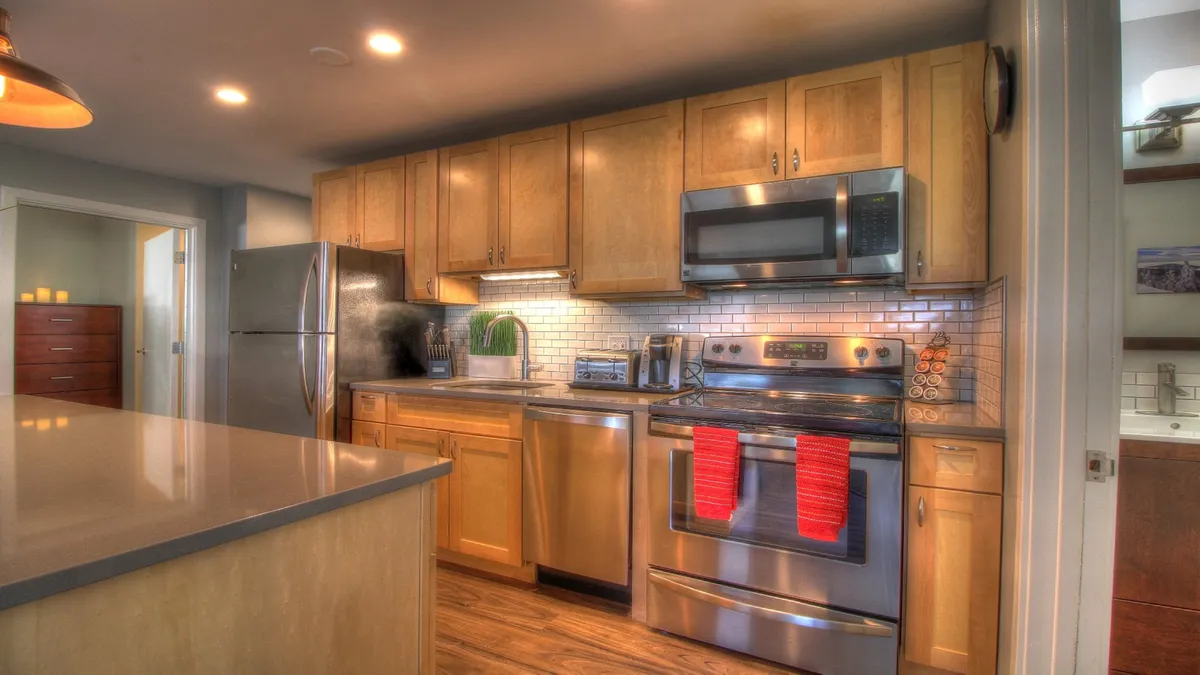 Featuring a modern kitchen with stainless steel appliances, bar seating, and red dish towels, this image captures an inviting space designed for cooking, entertaining, and sharing meals. The kitchen layout suggests both functionality and luxury, supporting activities like hosting dinner parties or baking with family.